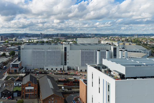 Aerial view of a large modern data center facility with industrial architecture rooftop cooling units and surrounding urban infrastructure in the United Kingdom. Aerial view of a large modern data center facility with industrial architecture rooftop cooling units and surrounding urban infrastructure in the United Kingdom.
