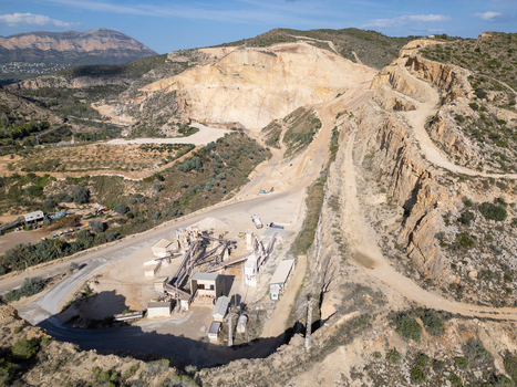 Aerial view of an open pit stone quarry with industrial processing machinery terraced rock faces and surrounding hilly landscape at Teulada Valencian Community Spain.