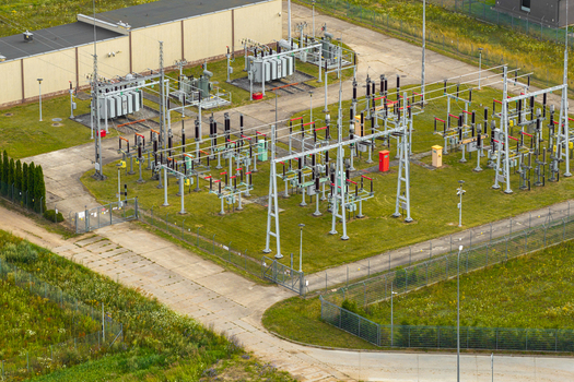 Aerial view of an electrical substation featuring transformers high voltage equipment and metal structures set within a fenced facility in Poland.