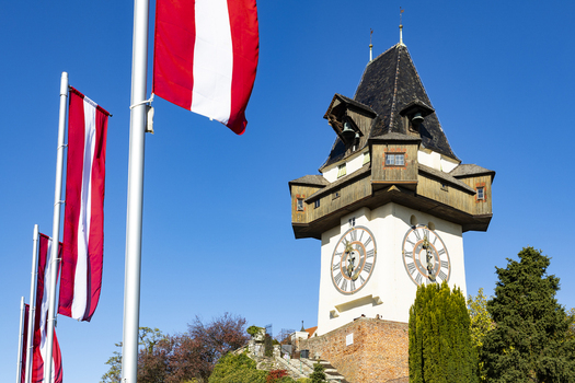 View of the iconic clock tower against a clear blue sky with Austrian flags waving gently in the breeze Graz Styria Austria. View of the iconic clock tower against a clear blue sky with Austrian flags waving gently in the breeze Graz Styria Austria.
