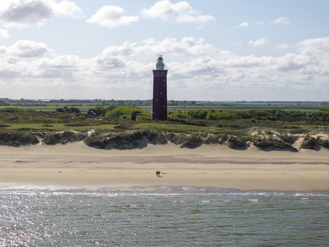 Aerial view of Westhoofd Lighthouse standing amidst coastal dunes and green fields near the sandy beach with two people walking along the shore Ouddorp Zuid Holland Netherlands. Aerial view of Westhoofd Lighthouse standing amidst coastal dunes and green fields near the sandy beach with two people walking along the shore Ouddorp Zuid Holland Netherlands.