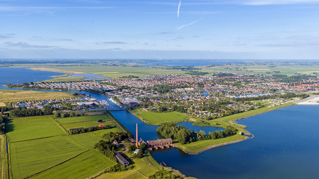 Aerial view of the historic Wouda pumping station with its red brick chimney surrounded by green fields canals and the IJsselmeer lake in Lemmer Friesland Netherlands.