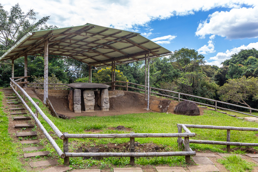 View of the ancient monolithic stone statues at San Agustin Archaeological Park protected by a wooden shelter in a lush green landscape in San Agustin Huila Colombia.