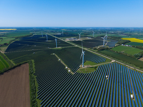 Aerial view of Chelveston Wind Farm featuring rows of solar panels and tall wind turbines across green fields under a clear blue sky in Wellingborough England United Kingdom. Aerial view of Chelveston Wind Farm featuring rows of solar panels and tall wind turbines across green fields under a clear blue sky in Wellingborough England United Kingdom.