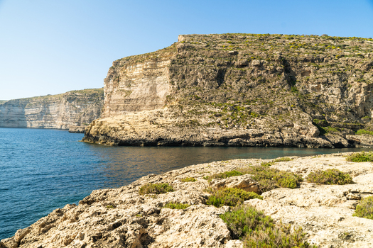 View of the rugged limestone cliffs and deep blue waters of Xlendi Bay under a clear sky Zebbug Gozo Region Malta.