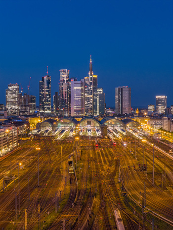 Aerial view of Hauptbahnhof central station with illuminated train tracks and the modern city skyline under a blue hour sky Frankfurt am Main Hessen Germany.