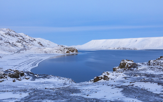 View of a serene lake reflecting the clear blue sky surrounded by snow covered mountains and rocky terrain Kleifarvatn Grindav&iacute;kurb&aelig;r Iceland.