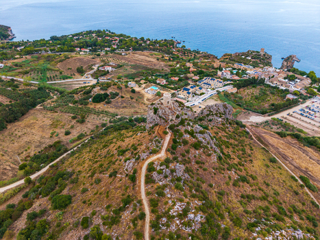 Aerial view of a historic coastal watchtower perched on a rocky hill with a winding path surrounded by Mediterranean vegetation and a coastal village in Palermo Sicily Italy. Aerial view of a historic coastal watchtower perched on a rocky hill with a winding path surrounded by Mediterranean vegetation and a coastal village in Palermo Sicily Italy.