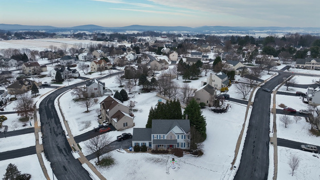 Aerial view of a suburban neighborhood covered in fresh snow featuring residential houses winding roads and distant hills under a winter sky in Lititz Pennsylvania United States.