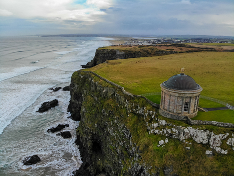 Aerial view of Mussenden Temple perched on a cliff edge overlooking the Atlantic Ocean with grassy fields and rocky coastline in Coleraine Northern Ireland United Kingdom. Aerial view of Mussenden Temple perched on a cliff edge overlooking the Atlantic Ocean with grassy fields and rocky coastline in Coleraine Northern Ireland United Kingdom.