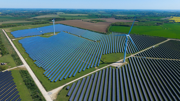 Aerial view of Chelveston Wind Farm featuring vast solar panel arrays and wind turbines across the green countryside in Wellingborough England United Kingdom. Aerial view of Chelveston Wind Farm featuring vast solar panel arrays and wind turbines across the green countryside in Wellingborough England United Kingdom.