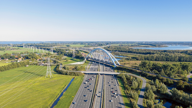 Aerial view of the Junction Muiderberg bridge spanning the A1 motorway surrounded by lush green fields power lines and water bodies in Muiderberg North Holland Netherlands. Aerial view of the Junction Muiderberg bridge spanning the A1 motorway surrounded by lush green fields power lines and water bodies in Muiderberg North Holland Netherlands.