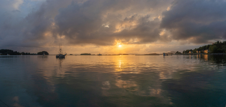 View of fishing boats anchored in a calm bay under a dramatic sunset with heavy clouds and golden light reflecting on the water United States. View of fishing boats anchored in a calm bay under a dramatic sunset with heavy clouds and golden light reflecting on the water United States.