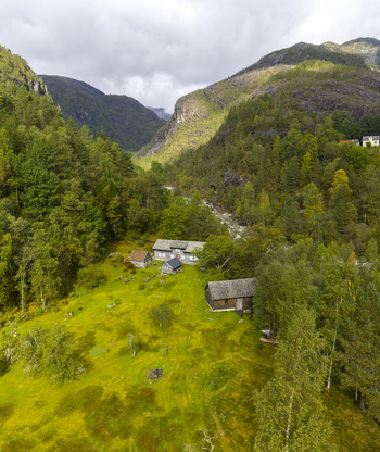 Aerial view of traditional wooden farmhouses nestled in a lush green valley surrounded by dense forests and steep mountains in Fjaera Vestland Norway. Aerial view of traditional wooden farmhouses nestled in a lush green valley surrounded by dense forests and steep mountains in Fjaera Vestland Norway.