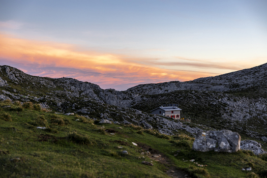 View of a cozy refuge nestled amidst the rugged rocky terrain bathed in the warm glow of the setting sun painting the sky with fiery hues Picos de Europa Asturias Spain.