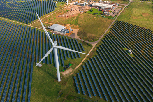 Aerial view of the Chelveston Renewable Energy site featuring a large wind turbine surrounded by extensive rows of solar panels and industrial infrastructure in Chelveston England United Kingdom. Aerial view of the Chelveston Renewable Energy site featuring a large wind turbine surrounded by extensive rows of solar panels and industrial infrastructure in Chelveston England United Kingdom.