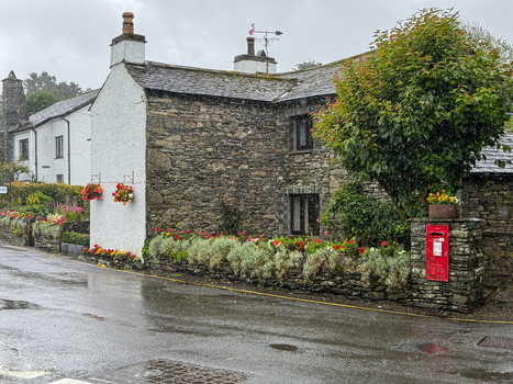 View of traditional stone cottages with flower boxes and a red post box along a wet street in Hawes England United Kingdom. View of traditional stone cottages with flower boxes and a red post box along a wet street in Hawes England United Kingdom.