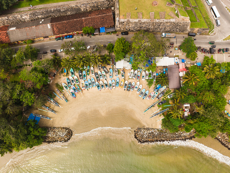 Aerial view of colorful fishing boats parked on a sandy beach cove surrounded by palm trees and the historic stone walls of the fort in Galle Southern Province Sri Lanka. Aerial view of colorful fishing boats parked on a sandy beach cove surrounded by palm trees and the historic stone walls of the fort in Galle Southern Province Sri Lanka.