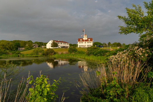View of a historic white building with a red roof reflecting in a calm pond surrounded by lush greenery in Edgartown Massachusetts United States.