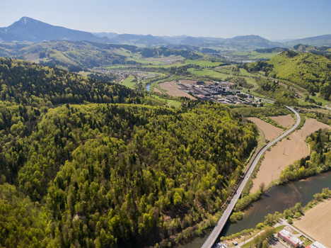 Aerial view of the Orava river winding through lush green forests and a valley with a bridge and industrial area under a clear blue sky Oravsky Podzamok Zilina Region Slovakia. Aerial view of the Orava river winding through lush green forests and a valley with a bridge and industrial area under a clear blue sky Oravsky Podzamok Zilina Region Slovakia.