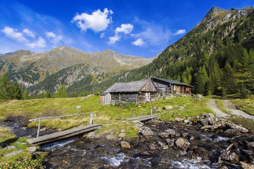 View of rustic wooden huts nestled amidst vibrant green meadows contrasted by rugged mountains under a bright sky Duisitzkarsee Styria Austria. View of rustic wooden huts nestled amidst vibrant green meadows contrasted by rugged mountains under a bright sky Duisitzkarsee Styria Austria.