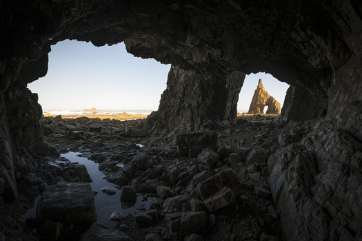 View of the rugged coastline and sea stacks through the opening of a dark sea cave at Playa de Campiechos Spain.