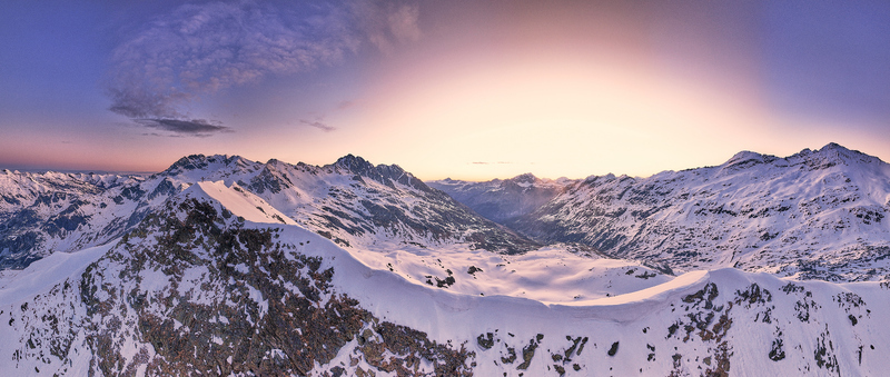 Aerial view of Vallespluga mountains covered in deep snow under a vibrant sunset sky in Lombardy Italy. Aerial view of Vallespluga mountains covered in deep snow under a vibrant sunset sky in Lombardy Italy.