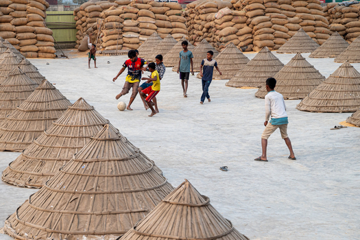 Brahmanbaria Bangladesh 24 January 2026 Aerial view of children playing football among conical grain covers and large stacks of sacks in a rural industrial area.