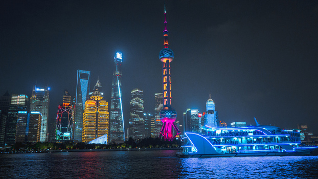 View of the illuminated Lujiazui skyline featuring the Oriental Pearl Tower and modern skyscrapers at night seen from the North Bund across the Huangpu River in Shanghai China.