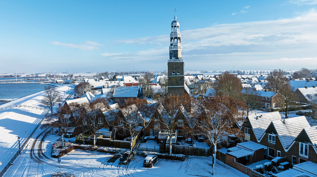 Aerial view of the historic church tower and snow covered rooftops of the town with the dike along the IJsselmeer in Hindeloopen Friesland Netherlands. Aerial view of the historic church tower and snow covered rooftops of the town with the dike along the IJsselmeer in Hindeloopen Friesland Netherlands.