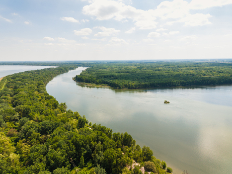 Aerial view of a wide river winding through a lush green forest under a bright sky with scattered clouds in Bratislava Bratislava Region Slovakia. Aerial view of a wide river winding through a lush green forest under a bright sky with scattered clouds in Bratislava Bratislava Region Slovakia.