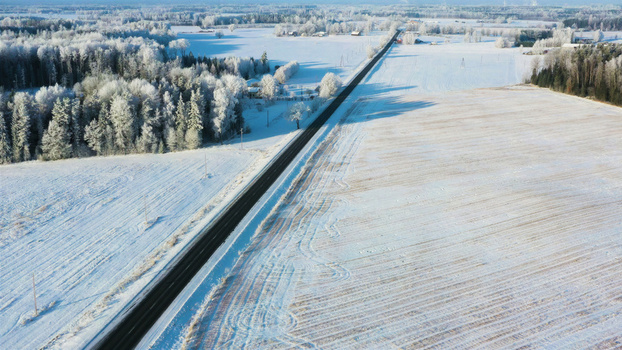 Aerial view of a straight asphalt road cutting through a vast snow covered landscape with frost covered trees and open fields in Latvia. Aerial view of a straight asphalt road cutting through a vast snow covered landscape with frost covered trees and open fields in Latvia.