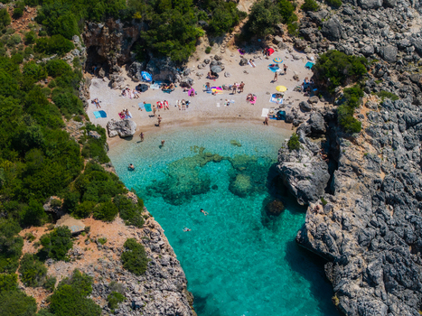 Aerial view of Aquarium Beach with turquoise water rocky cliffs and people sunbathing in Jala Vlore County Albania. Aerial view of Aquarium Beach with turquoise water rocky cliffs and people sunbathing in Jala Vlore County Albania.