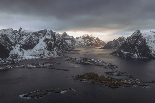 Aerial view of snow dusted peaks meet the dark waters casting long shadows over the quaint villages nestled along the rugged coastline Reinebringen Nordland Norway.