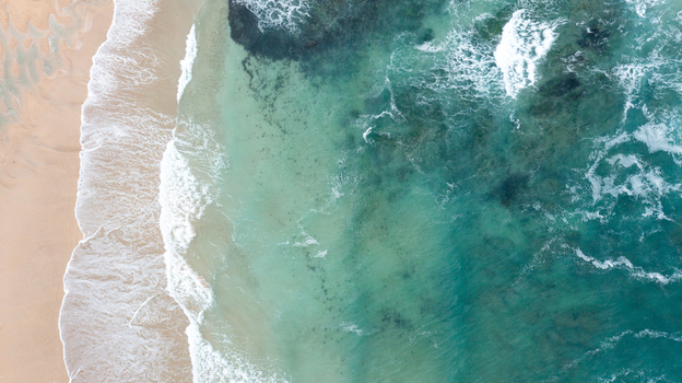 Aerial view of turquoise ocean waves crashing onto the sandy shore of Constantine Bay in Padstow Cornwall United Kingdom. Aerial view of turquoise ocean waves crashing onto the sandy shore of Constantine Bay in Padstow Cornwall United Kingdom.