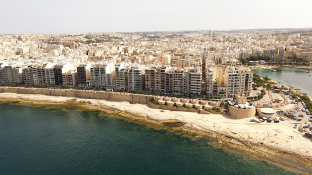 Aerial view of the coastal urban landscape featuring modern apartment buildings historic fortifications and a rocky shoreline in Malta. Aerial view of the coastal urban landscape featuring modern apartment buildings historic fortifications and a rocky shoreline in Malta.