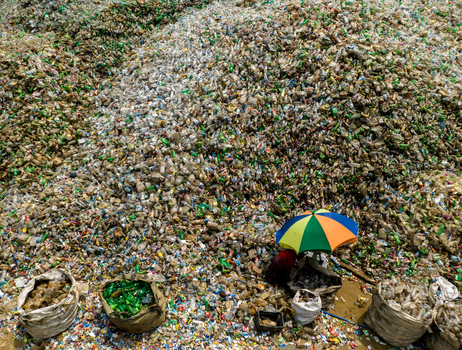 Aerial view of a worker sorting through a massive pile of plastic bottles at a recycling facility with large sacks and a colorful umbrella in Chattogram Chittagong Division Bangladesh.
