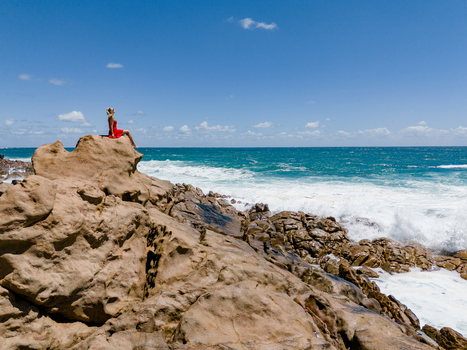 Aerial view of Injidup Natural Spa with a woman in a red dress sitting on the rocky coastline overlooking the turquoise Indian Ocean in Yallingup Western Australia Australia. Aerial view of Injidup Natural Spa with a woman in a red dress sitting on the rocky coastline overlooking the turquoise Indian Ocean in Yallingup Western Australia Australia.