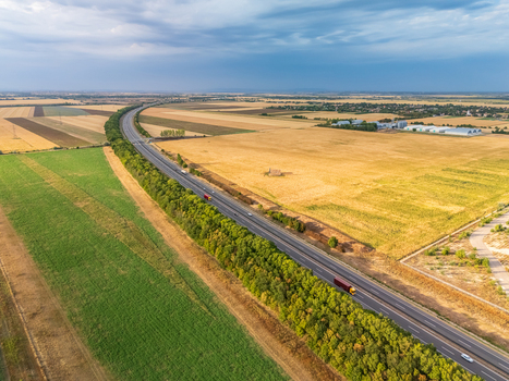 Aerial view of the M6 motorway near Ivancsa Hungary with traffic at an overpass through rural farmland grain fields industrial buildings and power lines. Aerial view of the M6 motorway near Ivancsa Hungary with traffic at an overpass through rural farmland grain fields industrial buildings and power lines.