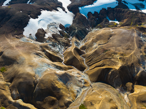 Aerial view of rugged mountains and snow patches meet in a symphony of brown white and grey carved by winding streams Iceland.