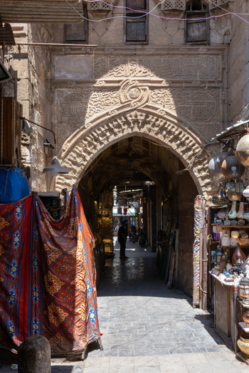 Cairo Egypt 20 April 2026 View of Khan el Khalili bazaar featuring an ornate stone archway with a person standing in the shadows among traditional lanterns and textiles. Cairo Egypt 20 April 2026 View of Khan el Khalili bazaar featuring an ornate stone archway with a person standing in the shadows among traditional lanterns and textiles.