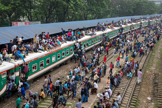 Dhaka Bangladesh 15 June 2018 View of Airport Railway Station with people sitting on train roofs and standing along the tracks under lush green trees. Dhaka Bangladesh 15 June 2018 View of Airport Railway Station with people sitting on train roofs and standing along the tracks under lush green trees.