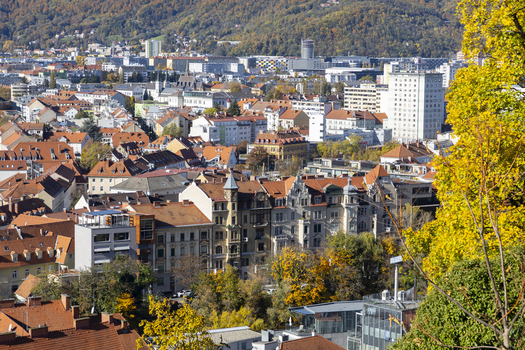 View of vibrant orange rooftops nestled among autumn trees juxtaposed against the modern skyline under a crisp blue sky Graz Styria Austria. View of vibrant orange rooftops nestled among autumn trees juxtaposed against the modern skyline under a crisp blue sky Graz Styria Austria.