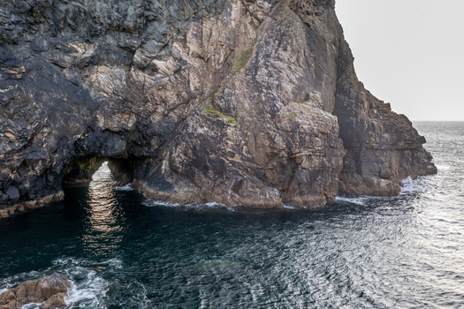Aerial view of Glenlough Bay featuring dramatic rugged cliffs and a natural sea arch with dark Atlantic waters in Ardara County Donegal Ireland.