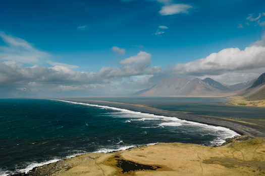 Aerial view of Stokksnes featuring a dramatic black sand beach rugged mountains and crashing ocean waves in Iceland.