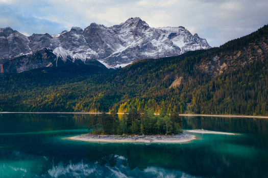 Aerial view of the turquoise waters of Eibsee lake with a small forested island and the snow capped Zugspitze mountain massif in Grainau Bavaria Germany. Aerial view of the turquoise waters of Eibsee lake with a small forested island and the snow capped Zugspitze mountain massif in Grainau Bavaria Germany.