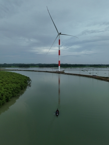 Aerial view of the Khurushkul wind turbine rising above the river with a small boat navigating the water surrounded by greenery in Cox s Bazar Chittagong Division Bangladesh. Aerial view of the Khurushkul wind turbine rising above the river with a small boat navigating the water surrounded by greenery in Cox s Bazar Chittagong Division Bangladesh.