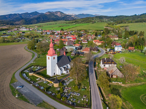 Aerial view of the historic Church of Saint Ladislaus with its red steeple and surrounding cemetery nestled among green fields and rolling hills in Liptovske Matiasovce Zilina Region Slovakia.