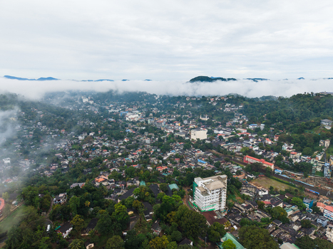 Aerial view of the urban landscape of Kandy nestled among lush green hills with mist rolling over the mountains under an overcast sky Kandy Central Province Sri Lanka. Aerial view of the urban landscape of Kandy nestled among lush green hills with mist rolling over the mountains under an overcast sky Kandy Central Province Sri Lanka.