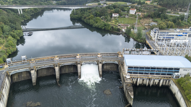 Aerial view of Subestacion Electrica Velle and the Velle Dam with water rushing through the spillway on the Minho River surrounded by green hills Ourense Ourense Spain.